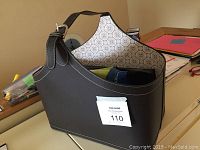 Black faux leather decorative basket with patterned interior and items inside on table