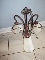 Overall view of ceiling light fixture showing metal frame, curved arms, and frosted glass shades on tiled floor against blue wall.