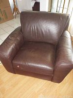 View of the brown leather armchair from the front, showing leather surface and cushioned armrests.