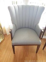 Front-facing view of the wing chair showing upholstery texture, wingback, and wooden arm trim.
