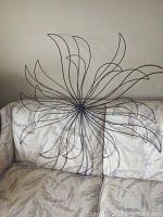 Full image of wire flower wall sculpture placed against a beige patterned couch for scale.