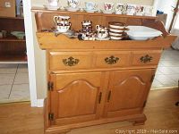 Front view of Roxton dry sink cabinet with cups and saucers on top, showing drawer and door layout
