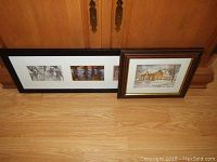 Two framed prints leaning against a wooden cabinet on a floor. One horizontal black frame with three small nature scenes, one brown square frame with winter cabin print.