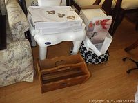 Photo showing two boxed serving platters, one stacked on top of the other, a boxed beverage dispenser behind them, and a wooden magazine rack in front with a heart cutout handle.