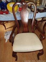 Front view of a mahogany captain's chair with an upholstered cream/beige seat cushion and curved backrest with detailed carvings