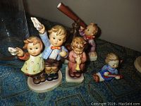 Four Hummel figurines displayed on patterned cloth, frontal view of all figures