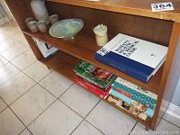 Wide view of wooden shelving containing books, glass bowl, stoneware jug, and four matching cups on tile floor.