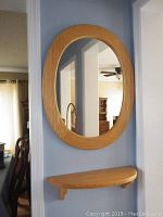 Pine oval mirror hung on a blue wall above a pine half-oval wall shelf, set in a home environment.