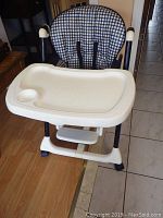 Front view of the infant high chair showing the checkered cushioned seat and feeding tray with cup holder.