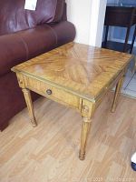 Front side view of Stanley wood end table next to a couch showing parquet wood top and single drawer with metal knob, fluted leg design visible.