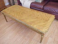 Photo of rectangular wood coffee table with parquet pattern top and fluted carved legs, on wood floor beside a leather couch.