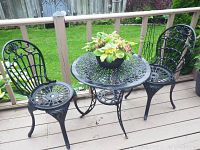 Full set of black metal bistro table with two matching chairs on a deck.