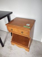 Front and angled view of wood veneer nightstand showing single drawer with brass knobs and lower open shelf.