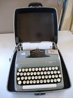 Front view of grey Smith-Corona portable typewriter inside its black case, paper loaded.