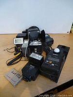 Image showing a group of camera flashes, the Minolta light meter, and movie lights arranged on a light wood surface.