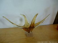 Front view of the gold-toned Art Deco glass sculpture placed on a wooden surface against a white background. Features curling upward and outward elongated points.