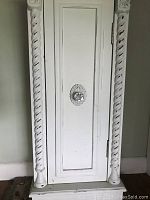 Front view of small white antique accent table with decorative twisted columns and glass knob on door, showing slight blemish top left corner.