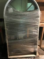 Front view of the new Harvey arch-top custom metal window, wrapped in clear plastic for protection. Shows the full window size and arch-top shape.