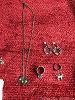 Multiple necklaces, hoop earrings, rings, and a small cat charm on red background