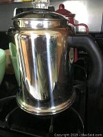 Farberware stainless steel coffee percolator with black plastic handle and clear glass knob lid on stove top.