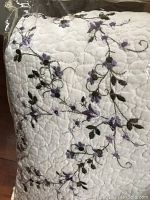 Close-up of quilt fabric showing white base with purple floral embroidery and detailed stitching.