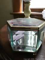Closed hexagonal glass jewelry box with brass-colored frame and floral design on lid