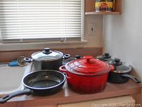View of all cookware items including red casserole dish, enamel crock, multiple black pots with lids and a frying pan
