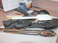 Various cooking utensils laid out including tongs, spatulas, and ladles with black and white handles
