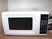 Front view of white microwave with door, control panel with digital clock display showing 10:59, numeric keypad and function buttons.