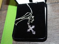 Full view of the cross necklace laid on a black velvet surface with green background showing the chain and pendant.