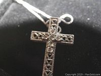 Close-up of front side of sterling silver cross pendant showing clear stones and heart cutouts on black background.