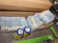 Photo of assorted batteries in plastic storage cases and loose on surface.