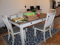 Set of four white wooden dining chairs around a table with upholstered seats.
