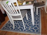 View of the blue and white geometric patterned medium-sized area rug under a white dining table with upholstered chairs, showing the pattern and size relative to furniture.