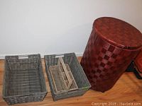 Photo showing two gray rectangular woven storage baskets, one utensil holder inside a basket, and large reddish-brown circular hamper on hardwood floor.