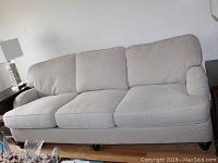 Front angled view of gray sleeper sofa with three seat and back cushions, fabric upholstery and dark wooden legs.