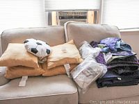 Four beige pillows arranged on couch along with a small soccer ball-shaped pillow and folded blankets.