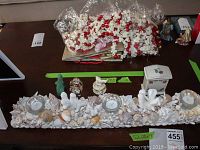 Photo of multiple decorative items on table including shell candle holder, dolphin trinket box, mini elephant figurines, Lenox Chinastone table clock, and some picture frames on the wooden table.