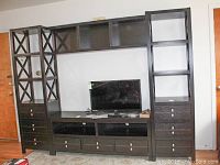 Full view of the U-shaped media shelf unit with drawers and lattice patterns on the left side shelving. TV placed in the center shelf (excluded from lot).
