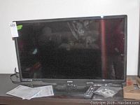 Front view of the 32 inch Sanyo flatscreen TV showing screen, base, remote, and instruction manual.
