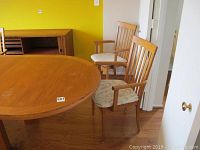 Set including six teak captain's chairs surrounding a wooden table, showing their armrests, slatted backs, and fabric padded seats.
