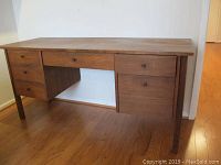 Front view of wooden desk showing five drawers and missing pull on right bottom drawer, wood floor setting