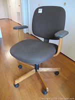 Front view of the fabric office chair showing seat, backrest, wooden arm supports, and caster wheels