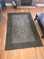 Full view of rectangular green shag rug laid out on wooden floor, showing color and design pattern.