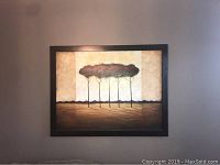 Front view of large painting mounted on wall depicting stylized trees with long shadows under a beige and brown background in a dark wooden frame.