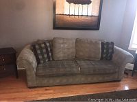 Front view of green couch with cushions, placed between two end tables, wall painting above.