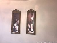 Two framed metal wall art panels depicting wine bottles and glasses against a wall.