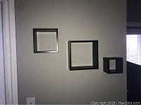 Three espresso shadow boxes mounted on wall in varying sizes with deep recessed frames and no glass front.