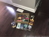 Photo of 11 assorted books on hardwood floor with a basket, featuring multiple Dean Koontz novels and others.