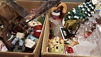 Two boxes of assorted Christmas decorations including ornaments, Santa hats, figurines, and a ceramic Christmas tree with lights
